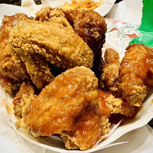 A basket of Harold's Chicken Shack West Loop's fried chicken wings, some coated in sauce, with fries.