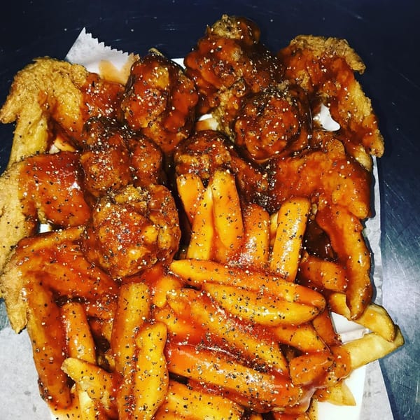 Harold's Chicken Shack wings and fries, drenched in sauce and sprinkled with pepper.