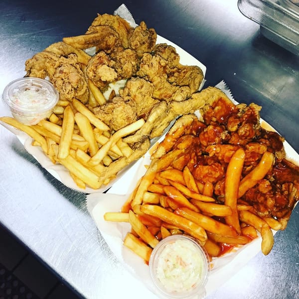 Two trays of Harold's Chicken Shack wings and fries, one plain and one sauced.