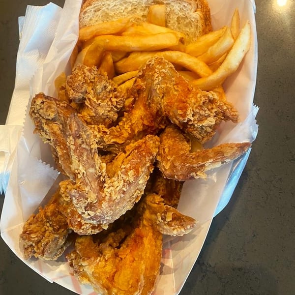 Harold's Chicken Shack's fried chicken wings and french fries in a white paper basket.